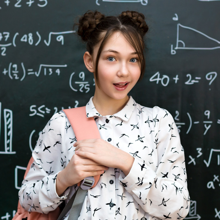 DDD-2024_WEB_TVO_LEARN Photo of a female teenager, standing in front of a blackboard with various math equations, holding a pink backpack strap on her shoulder.