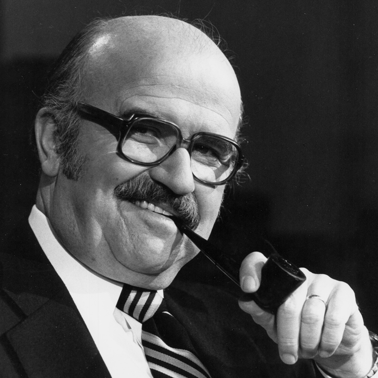 TVO_SNAM Black and white photo of Elwy Yost, host of Saturday Night at the Movies and Magic Shadows, holding a pipe to his mouth and smiling.