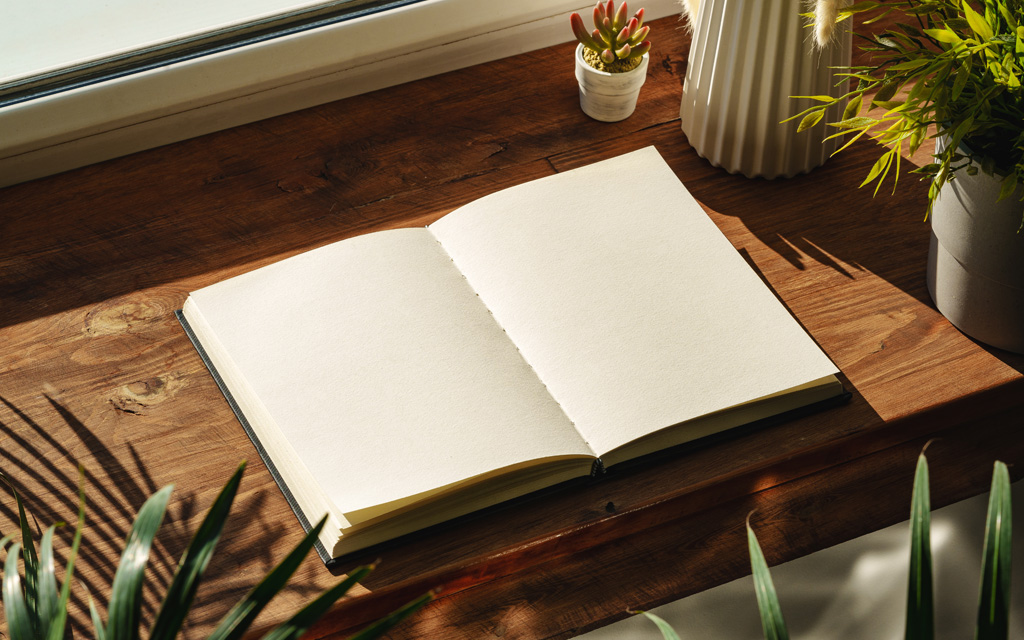 Photo of a notebook open by the window on wooden windowsill in sunlight.